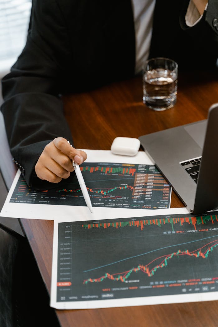About Close-up of a business analyst reviewing printed financial graphs and charts at an office desk.